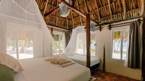 Une chambre avec un toit de chaume, deux lits équipés de moustiquaires et une vue sur la plage.