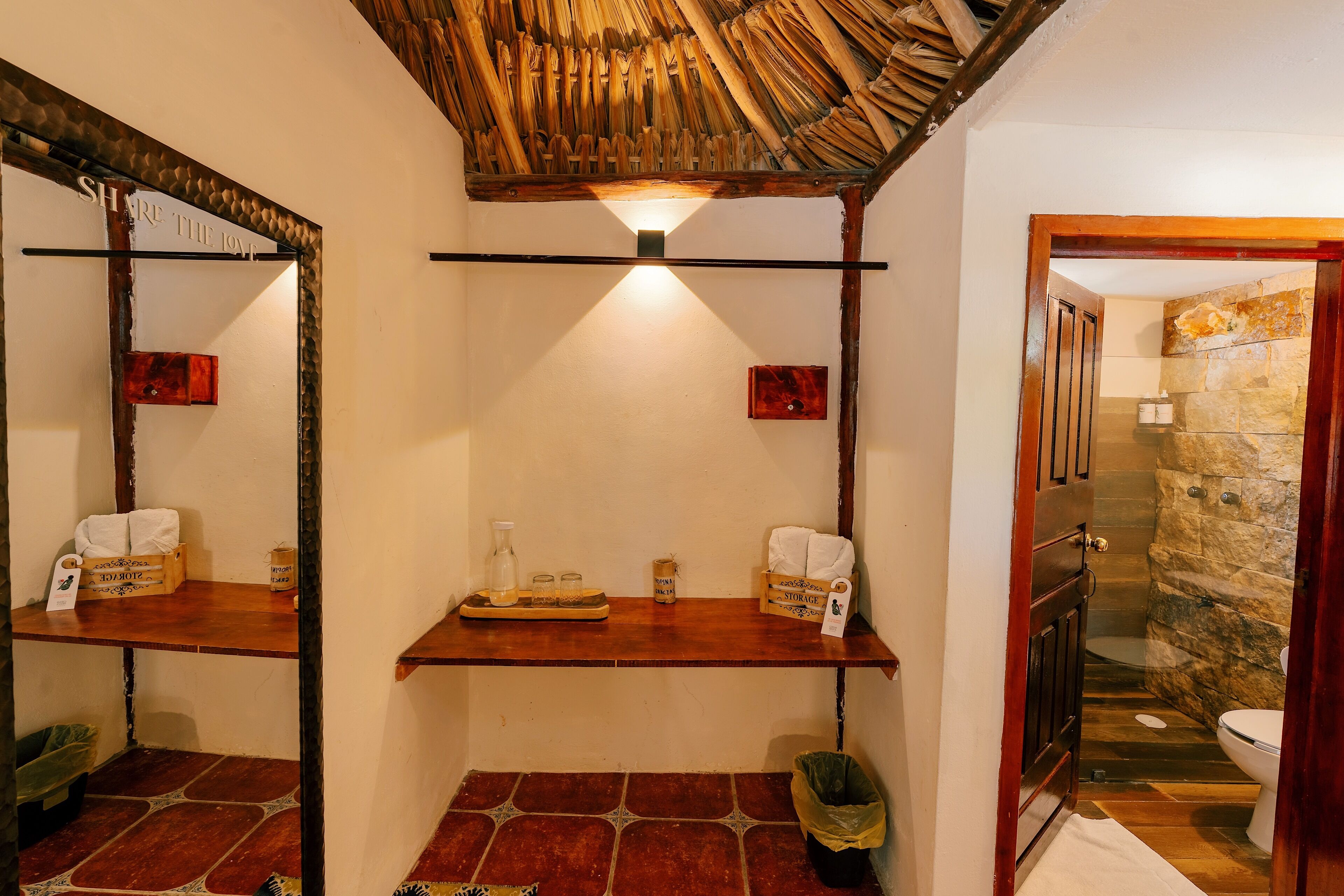 A bathroom with a wooden ceiling, a mirror, a shelf with toiletries, and a stone wall.