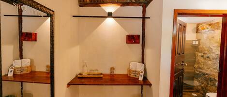 A bathroom with a wooden ceiling, a mirror, a shelf with toiletries, and a stone wall.