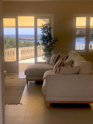 A living room with a beige sofa, a potted plant, and a view of the sea through large windows. - Villa with sea views, 4 bedrooms, free WIFI (Binisafuller)