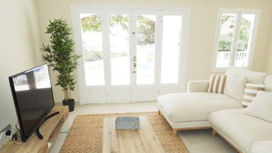 Een woonkamer met een flatscreen televisie, een houten salontafel, een witte bank en een grote potplant.