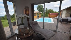 Ein modernes Zimmer mit Glastür zum Poolbereich, einer Liege und einem runden Tisch mit Blumenvase.
