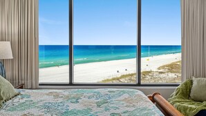 Quarto de hotel com uma janela ampla e vista para a praia.