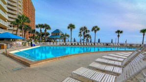 Uma área de piscina com espreguiçadeiras, um edifício com varandas e palmeiras.