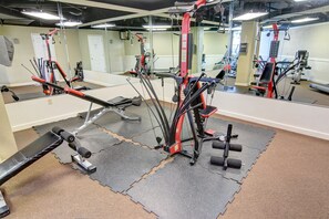 Ein Fitnessraum mit verschiedenen Trainingsgeräten, einem großen Spiegel und einem Teppichboden.