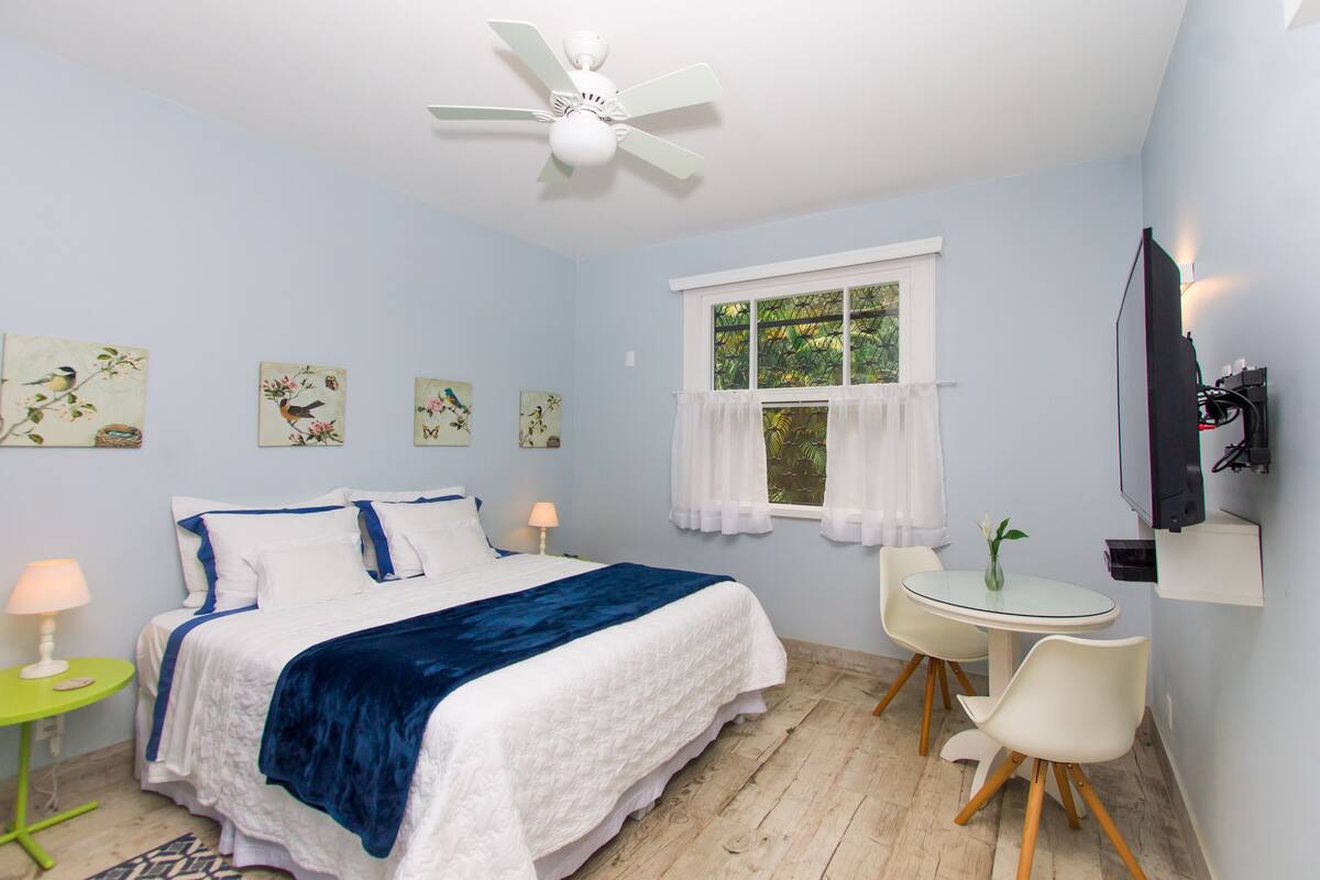 Quarto com cama, escrivaninha, cadeira, ventoinha no teto e obras de arte na parede.