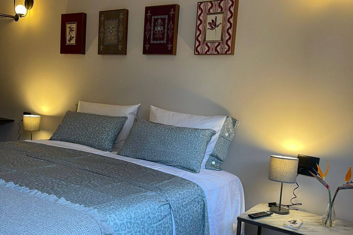 Quarto com cama, abajures, mesa de cabeceira, relógio e quadros na parede.