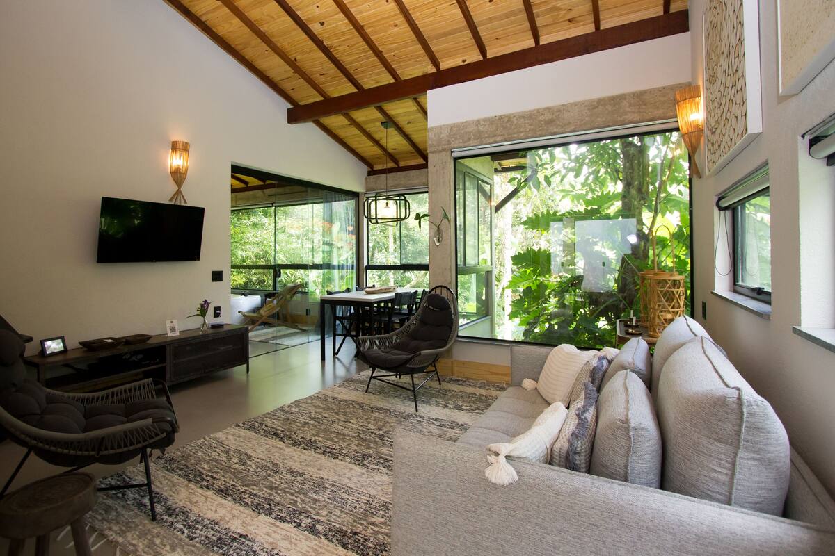 Uma sala de estar moderna com uma janela ampla, televisão de tela plana, sofá e área de jantar.