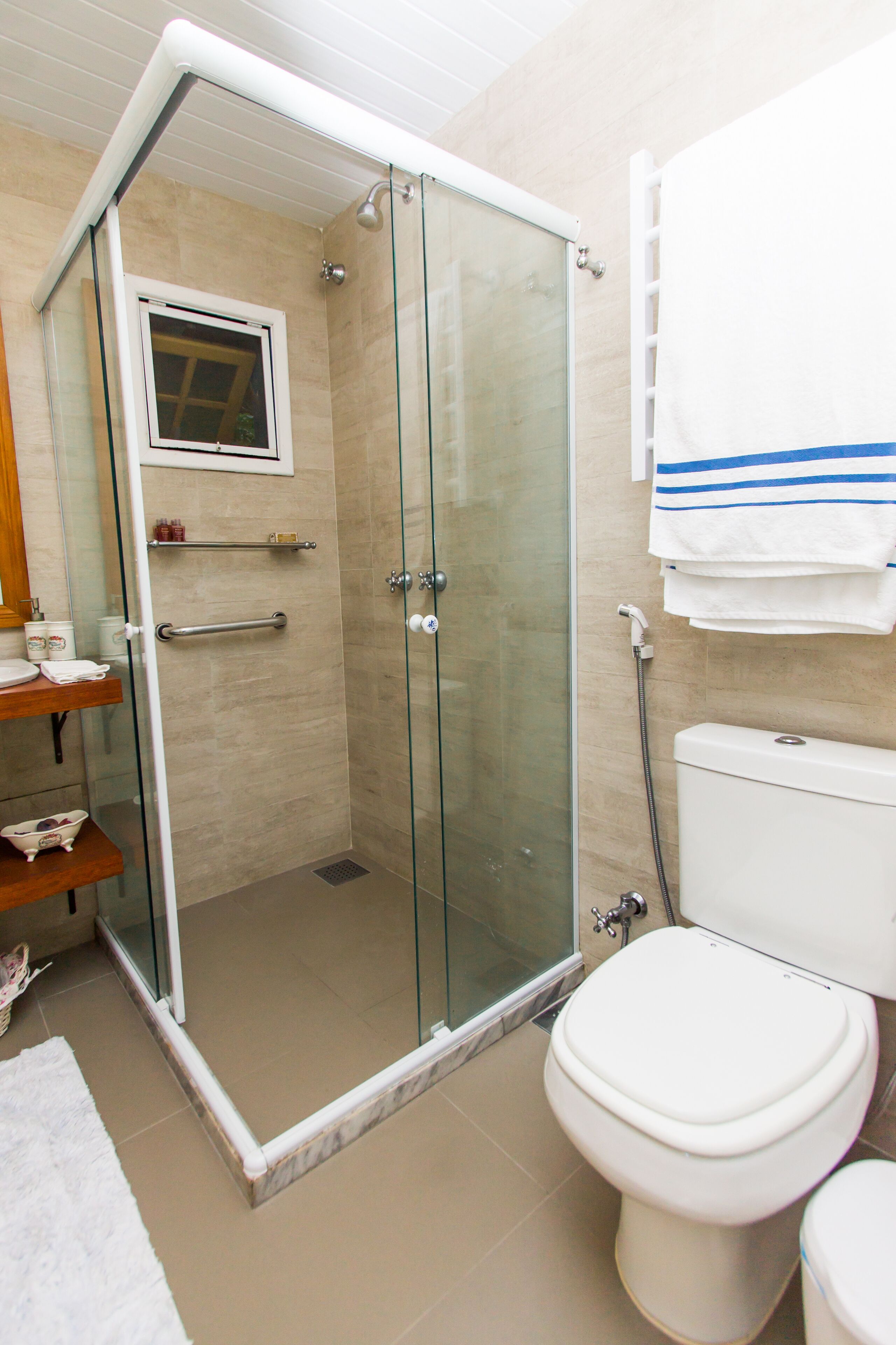 Un baño con ducha de vidrio, inodoro y lavamanos con toallero.