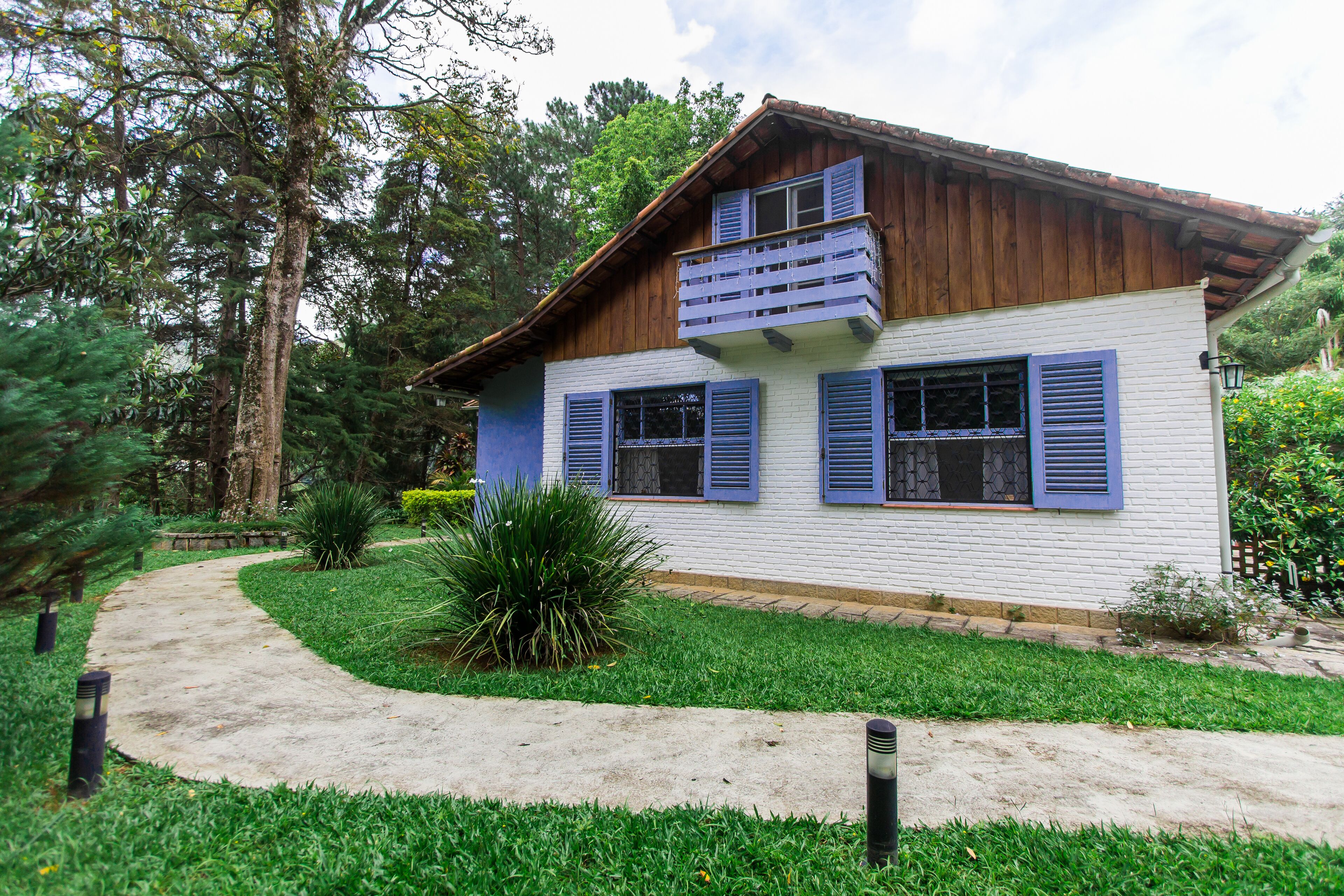 A two-story house with a white exterior and blue shutters, surrounded by a well-maintained garden and a curved pathway.