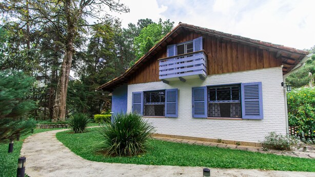A two-story house with a white exterior and blue shutters, surrounded by a well-maintained garden and a curved pathway.