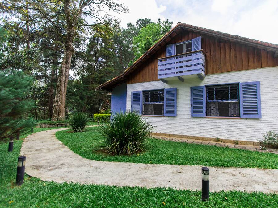 A two-story house with a white exterior and blue shutters, surrounded by a well-maintained garden and a curved pathway.