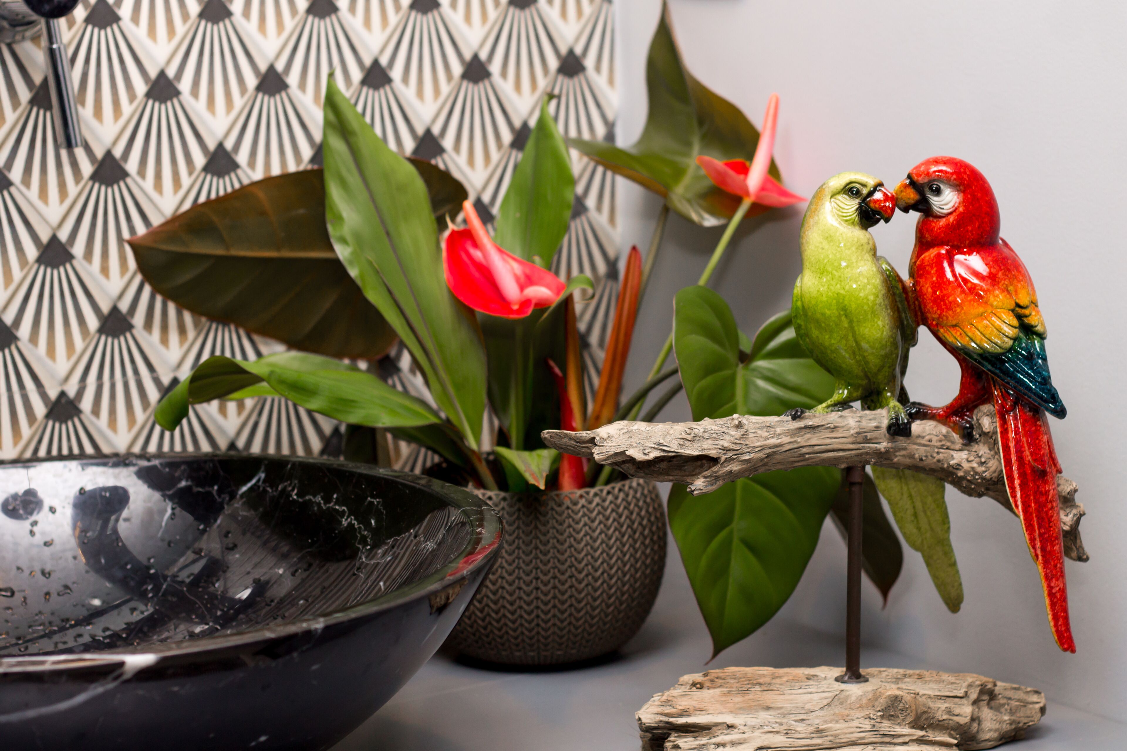 Dos figuras coloridas de guacamayos posadas en una rama, una planta en maceta y un cuenco decorativo.