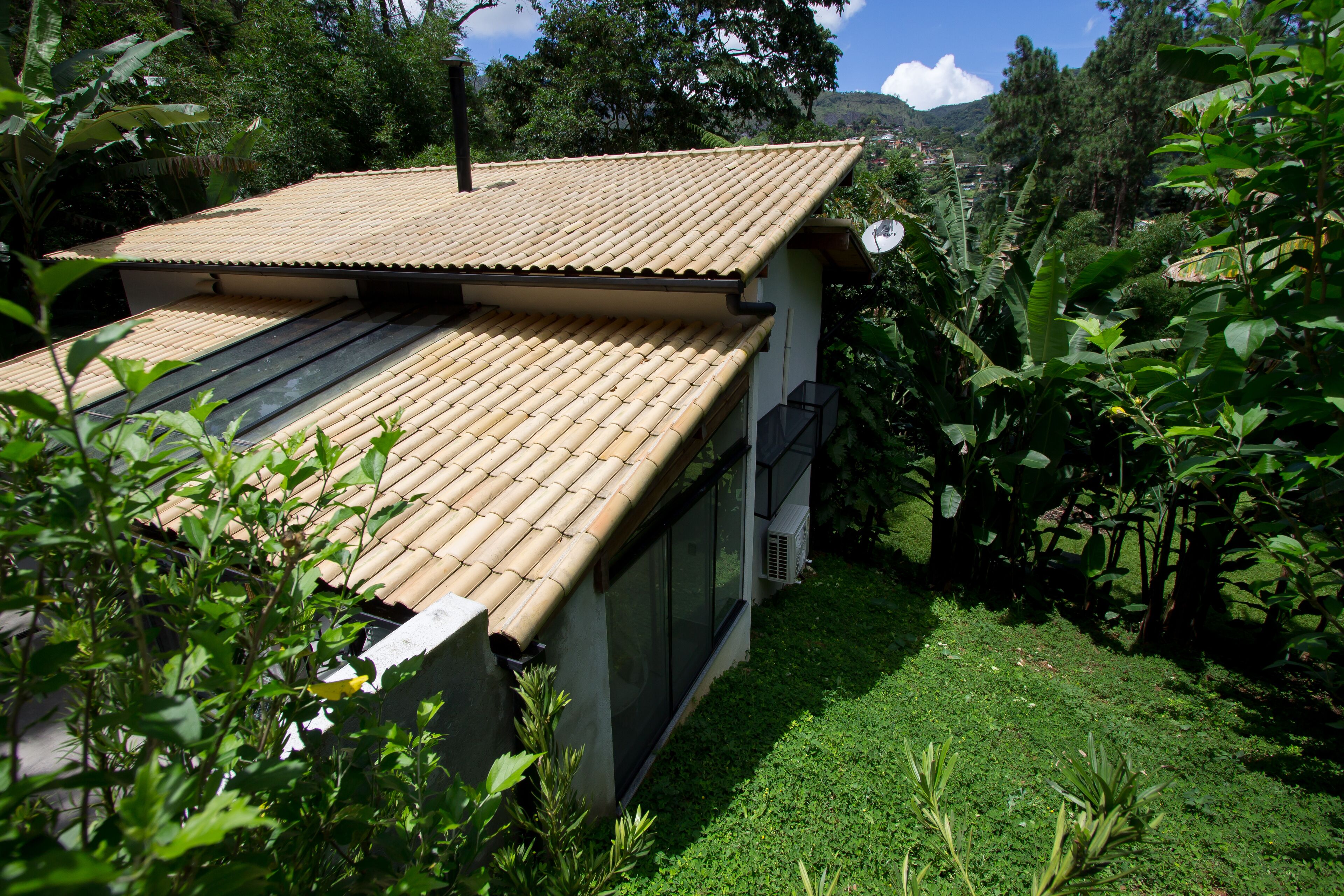 Ein Haus mit Ziegeldach, umgeben von üppiger Vegetation und einer hügeligen Landschaft im Hintergrund.