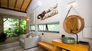 A modern living room with a grey sofa, wooden bench, and a round wooden table with a green bowl. - Pousada Chácara Aracê (Petrópolis)