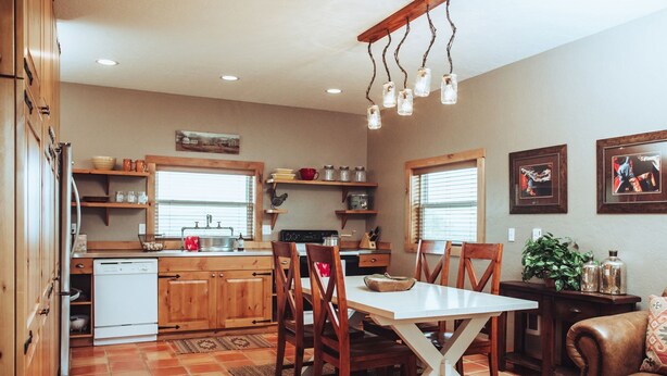 A kitchen with wooden cabinets, a white dishwasher, and a dining table with chairs. There are hanging lights above the table and a window with blinds. - 1- Bedroom 1- Bathroom Ranch Guest house. (Ellensburg)