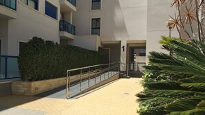 A modern building with a paved courtyard, a metal railing, and a hedge.