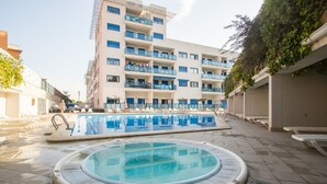 A hotel with a swimming pool and a hot tub, surrounded by lounge chairs and umbrellas.