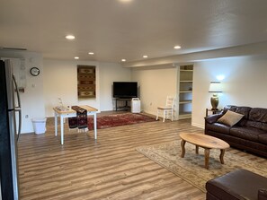 A living room with a wooden floor, a brown leather sofa, a TV, a small table, and a chair.