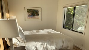 Une chambre à coucher avec un lit, une table de chevet, une lampe, une fenêtre et un tableau au mur.