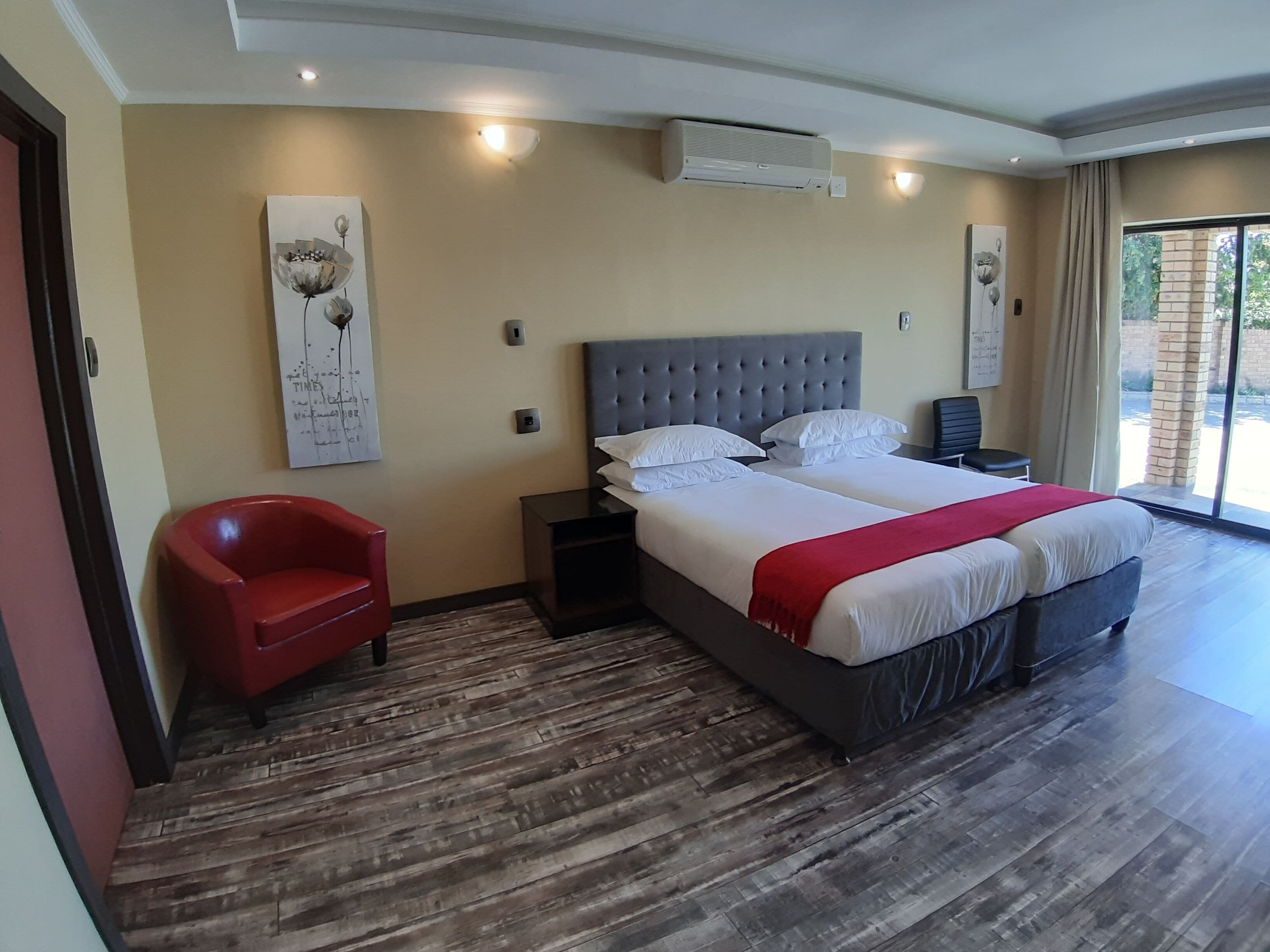 A modern bedroom with a large bed, a red chair, a bedside table, and a wall-mounted air conditioner.