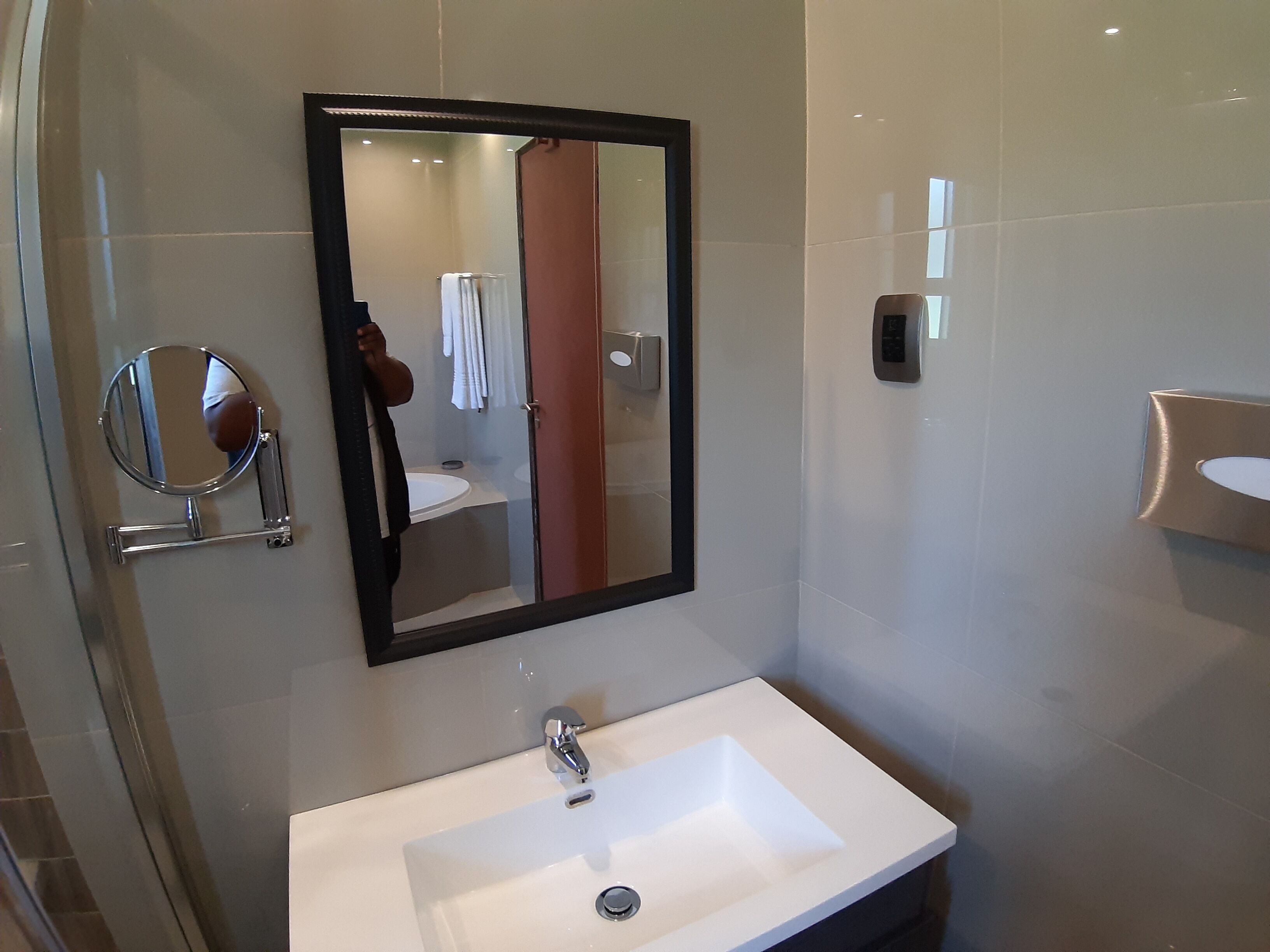 A bathroom with a large mirror, a sink, and a towel rack.