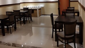 A hotel dining area with multiple tables and chairs, a kitchen area in the background, and a door to the right. - Citystay Ladybrand (Mantsopa)
