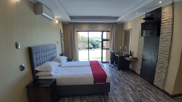A hotel room with two beds, a desk, a chair, a TV, and a large window with a view of greenery. - Citystay Ladybrand (Mantsopa)