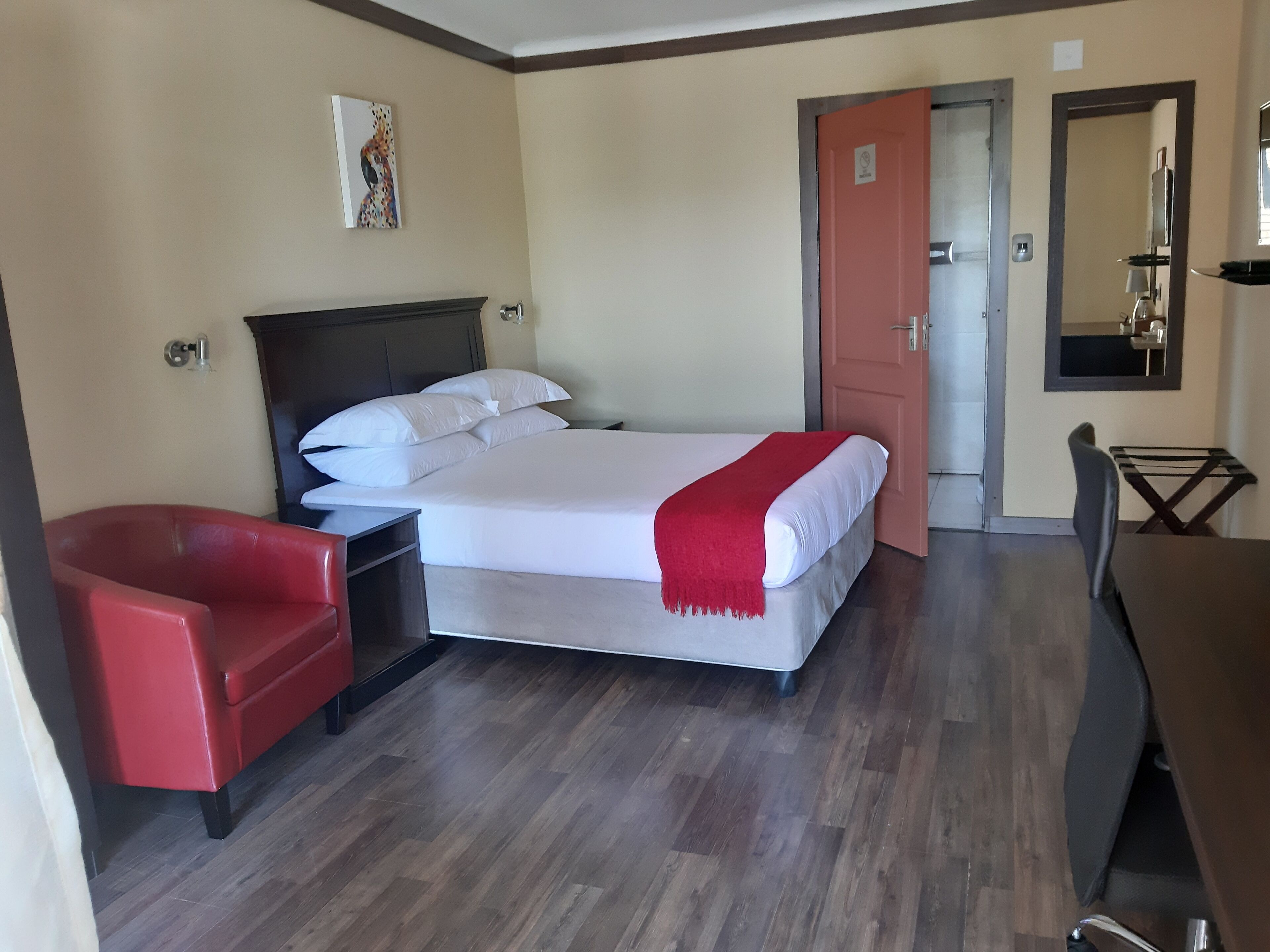 Une chambre d’hôtel avec un lit, une chaise rouge, un bureau et une porte donnant sur une autre pièce.