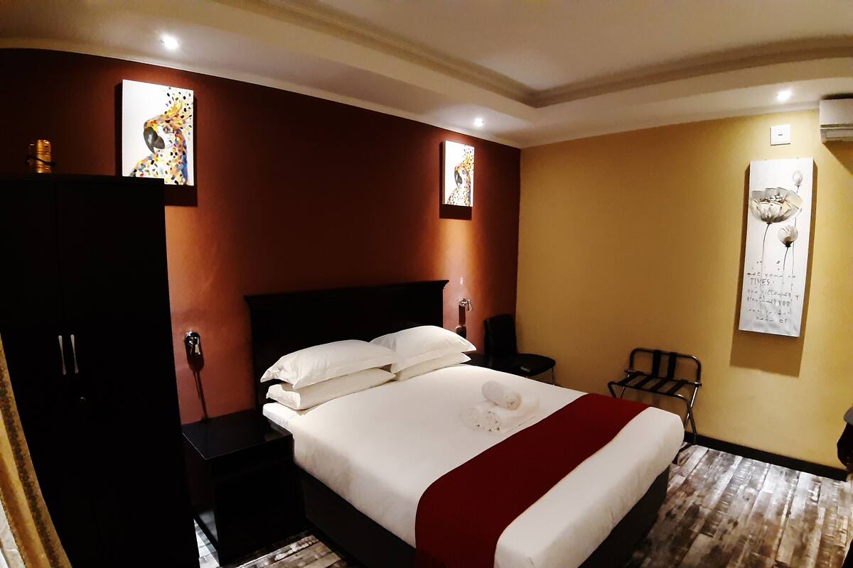 Une chambre d’hôtel avec un grand lit, un plancher en bois, une tête de lit sombre et des œuvres d’art accrochées aux murs.
