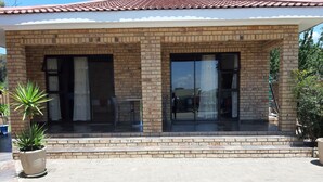 A covered patio area with a brick facade, large sliding glass doors, and potted plants. - Citystay Ladybrand (Mantsopa)
