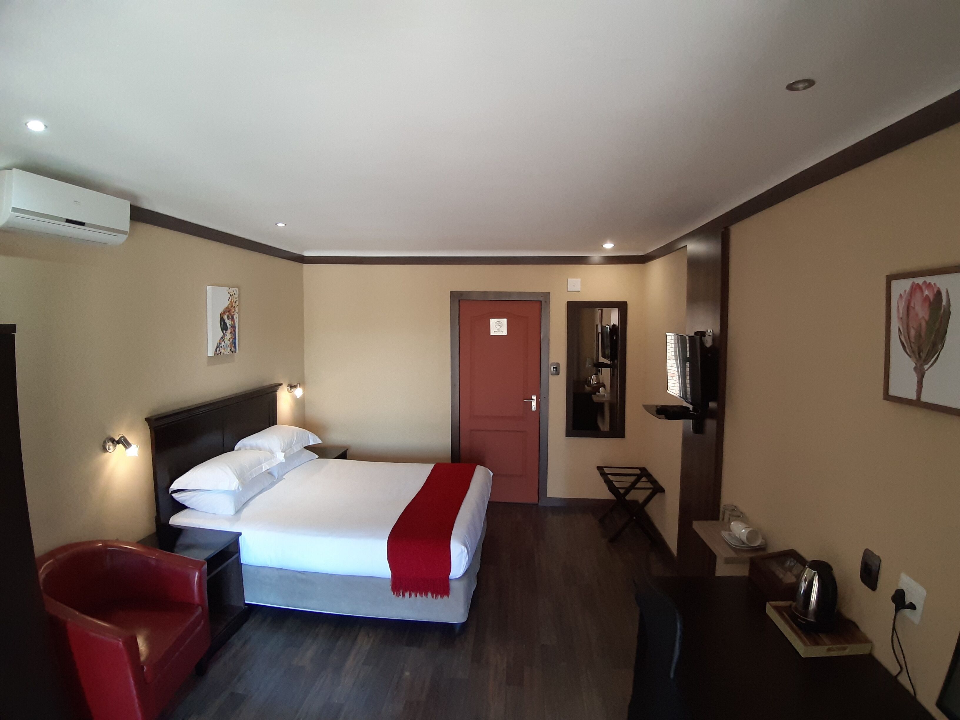 Una habitación de hotel con una cama, una silla roja, un televisor y un espejo.