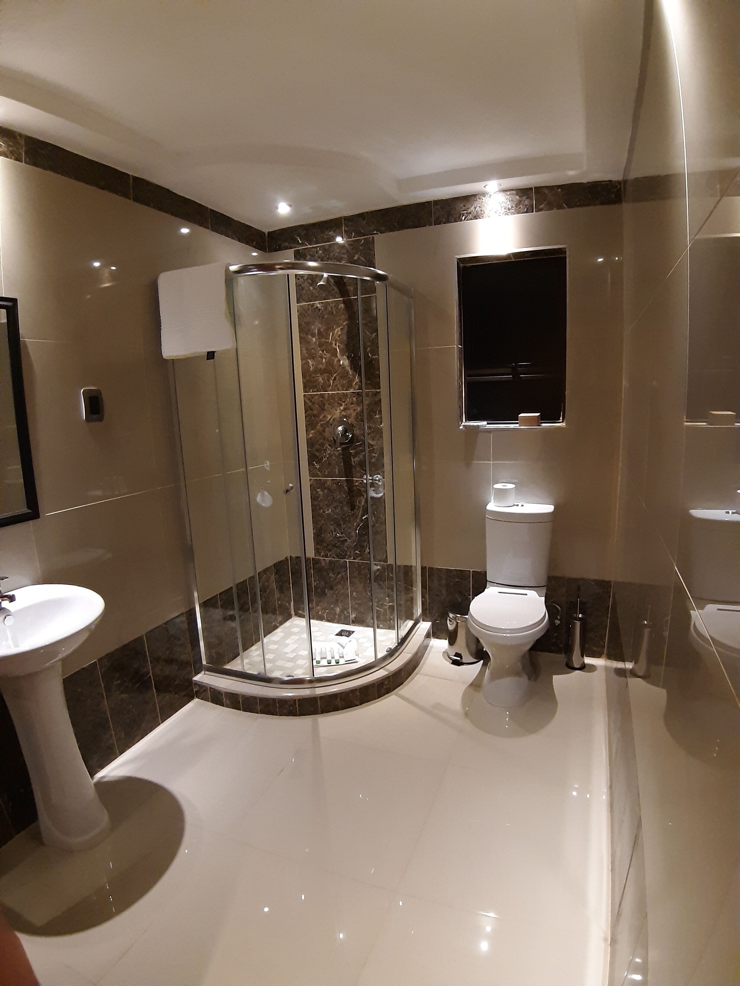 Un bany modern amb dutxa protegida per vidre, un lavabo amb pedestal, un vàter i un mirall sobre el lavabo.