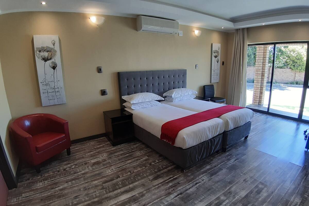 Une chambre d’hôtel moderne avec un grand lit, un fauteuil rouge, un plancher en bois et des œuvres d’art accrochées aux murs.