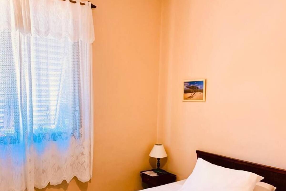 A neatly made bed with white linens and a striped blanket, a bedside lamp, and a small painting on the wall.