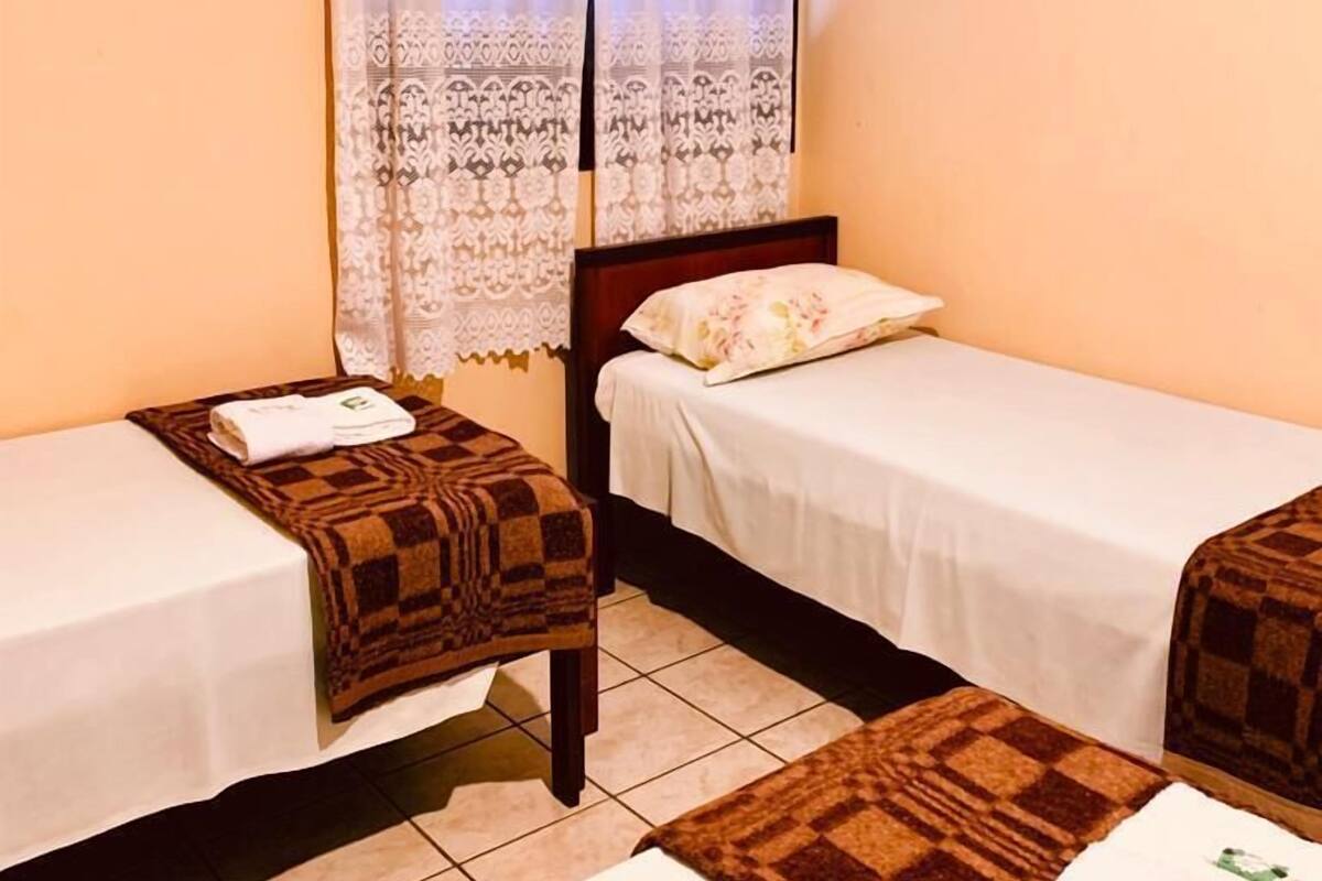 A small, cozy room with two single beds, a wooden nightstand, and a window with a lace curtain.