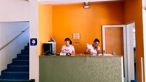 Een receptiebalie met twee medewerkers, een trap en een deur aan de rechterkant.