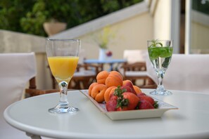 A table with a glass of orange juice, a glass of water with mint, and a plate of fruit including strawberries and apricots.