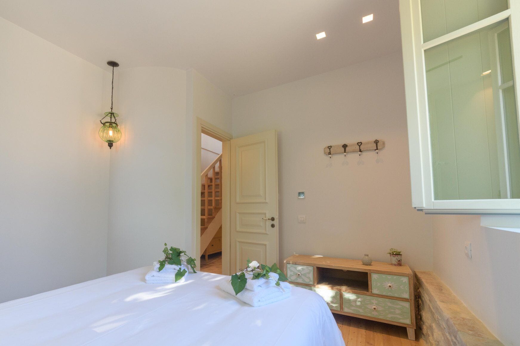 Une chambre à coucher comprenant un lit, des tables de chevet, un luminaire suspendu, une commode en bois et un escalier menant à une autre pièce.
