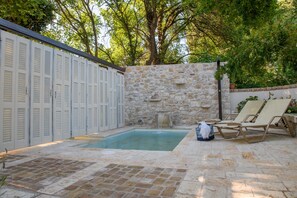 A stone-walled pool area with lounge chairs and a stone wall with shutters.