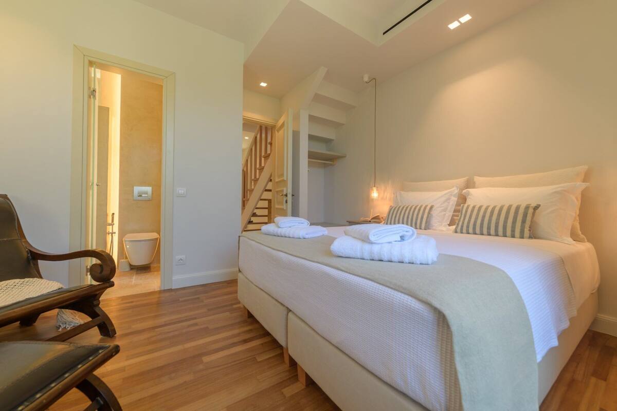 A bedroom with a large bed, a chair, a staircase, and a bathroom.