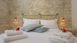 A bed with white linens, two pillows, and a rose. There are two bedside lamps and a stone wall behind the bed. - Carpofoli Corfu (Corfu)