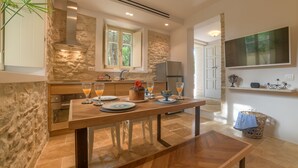 A modern kitchen with stone walls, a wooden dining table, and a built-in oven. - Carpofoli Corfu (Corfu)