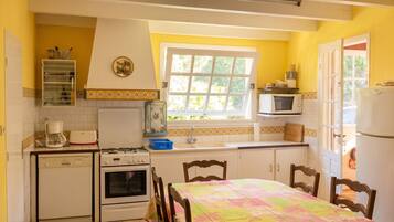 A compact kitchen with a dining area, featuring a stove, oven, microwave, and a window with a view.
