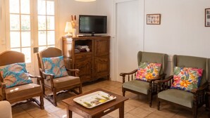 A living room with two wooden armchairs, a television on a cabinet, and a table with a tray. - Homerez - Cozy House in Vielle-Saint-Girons (Vielle-Saint-Girons)