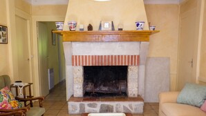 A living room with a fireplace, a sofa, a chair, a table, and a hallway. - Homerez - Cozy House in Vielle-Saint-Girons (Vielle-Saint-Girons)