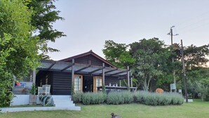Une maison en bois avec un porche, un petit jardin agrémenté d’une statue et un ciel dégagé.