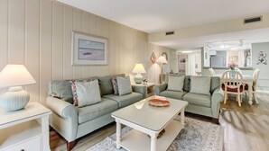 Un salon avec deux canapés vert clair, une table basse blanche et un coin repas comprenant une table et des chaises blanches.