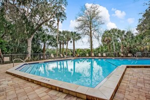 A rectangular swimming pool with a tiled edge, surrounded by lounge chairs and a brick patio.