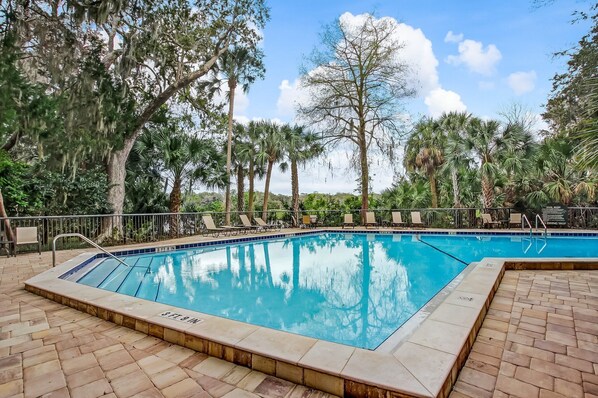 A rectangular swimming pool with a tiled edge, surrounded by a brick deck, and shaded by trees. - Cozy 2 bed/2 bath, Steps to The Beach, 2021 Beachwood (Amelia Island)